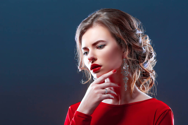 Close-up portrait of silly pretty feminine redhead woman with earrings, red lipstick and black dress, look from under forehead flirty, seducing someone acting clueless and dumb, red background - Photo, image
