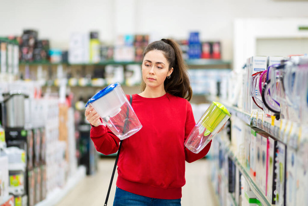 Una joven mujer caucásica elige entre dos jarras con filtro de agua en una tienda de electrodomésticos. - Foto, imagen