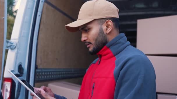 Genç Hintli adam teslimat siparişini kontrol etmek için tablet kullanıyor. Karton kutularla kamyon yükleniyor - Video, Çekim