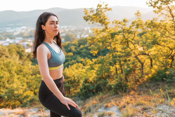 Sporty young woman resting during training. In the background plants and views of the settlements. The concept of sport, healthy lifestyle. - Photo, Image