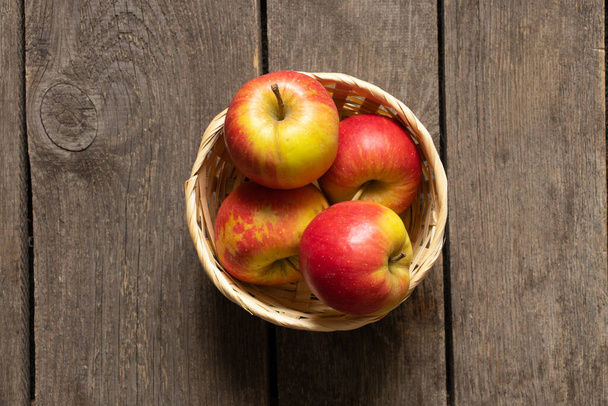 спелые яблоки лежат в плетеной соломенной корзине на деревянном фоне крупным планом - Фото, изображение