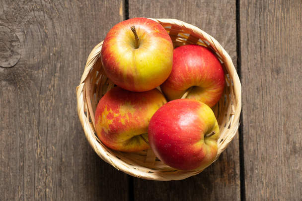 manzanas maduras se encuentran en una canasta de paja de mimbre sobre un fondo de madera de cerca - Foto, Imagen