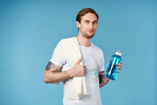 hombre en blanco camiseta tatuajes en sus brazos agua botella fitness estilo de vida - Foto, imagen
