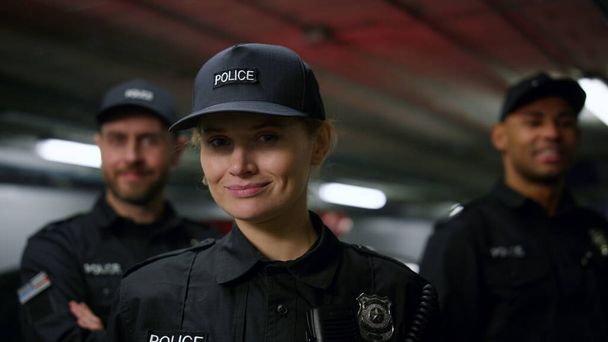 Hymyilevä poliisinainen katselee kameraa. Poliisi poseeraa kollegoidensa kanssa - Valokuva, kuva