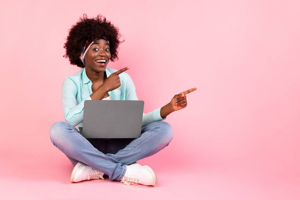 Veselý černošky žena s notebookem ukazující prsty ven, růžové pozadí - Fotografie, Obrázek