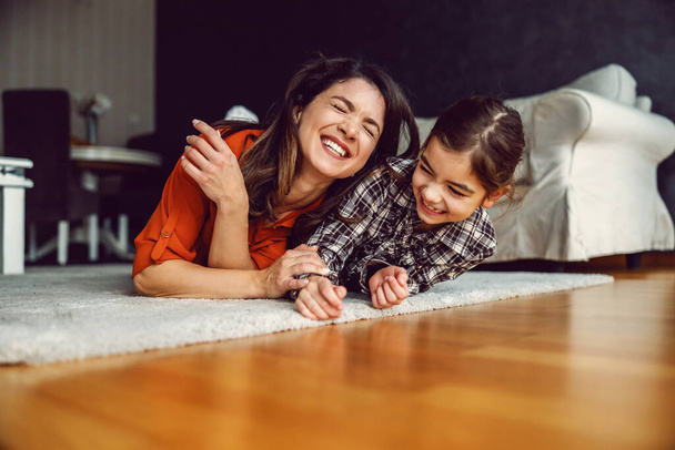 happy mother and daughter lying down on the floor at home and laughing. Love is only important thing for happy family. - Φωτογραφία, εικόνα