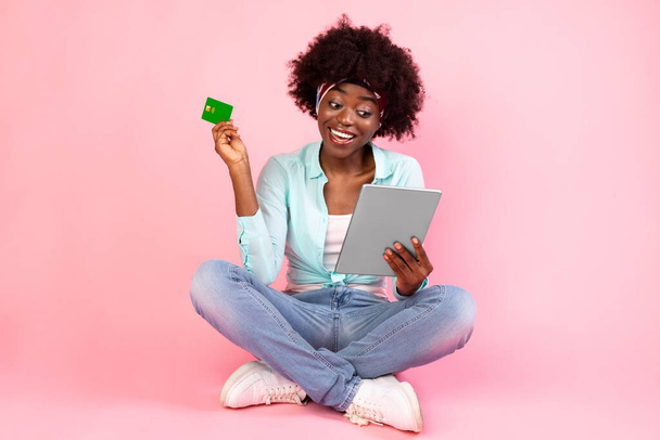 Mujer africana feliz con tarjeta de crédito usando tableta, fondo rosa - Foto, Imagen