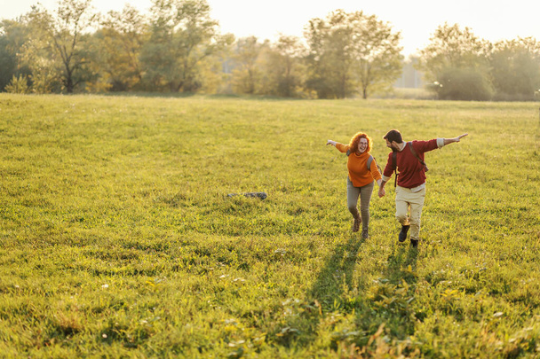 Young happy couple in love holding hands and running on meadow. It's a beautiful sunny autumn day. Freedom. - 写真・画像