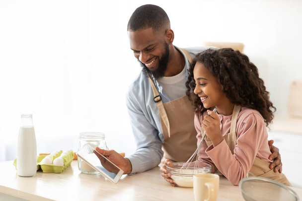 Black man and girl cooking in the kitchen using tablet - Photo, Image