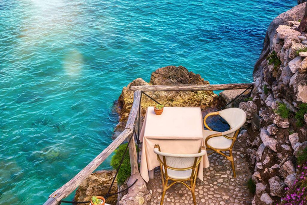 Ένα όμορφο τραπέζι για δύο σε μια απομονωμένη παραθαλάσσια τοποθεσία δίπλα στα ρηχά γαλάζια νερά της ακτής Αμάλφι στην Ιταλία. - Φωτογραφία, εικόνα