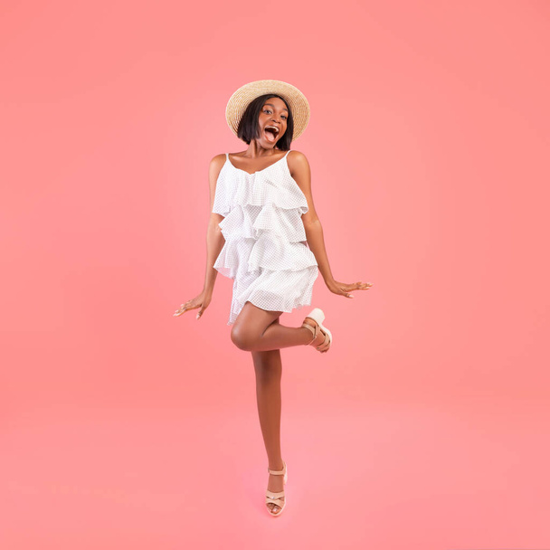 Full length portrait of fashionable black woman in lovely dress and straw hat on pink studio background - Foto, afbeelding
