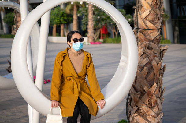 Eenzame Aziatische vrouw op een schommel stoel buiten het dragen van gezichtsmasker en sociale afstand in het openbaar - Foto, afbeelding