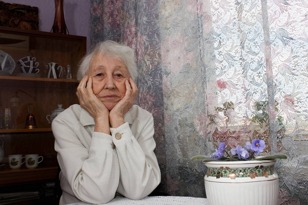 Пожилая одинокая женщина в депрессии, сидя за столом дома - Фото, изображение
