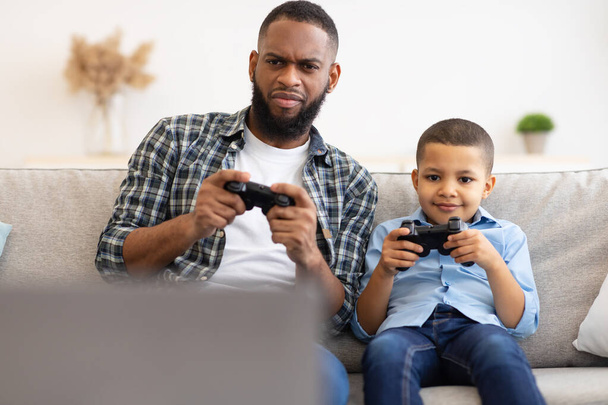 Fekete apa és fia együtt videojátékoznak otthon ülve - Fotó, kép