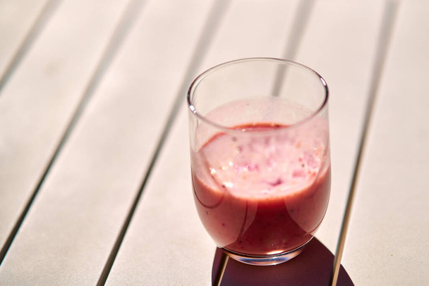 Gyümölcs smoothie piros színű fehér asztal alatt napfény - Fotó, kép