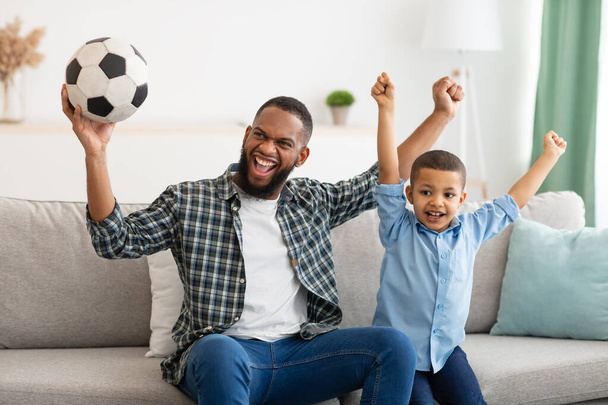 Радісний тато і син дивиться футбол гри на телебаченні в приміщенні
 - Фото, зображення