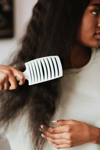 Una femmina africana spazzolando i suoi lunghi capelli neri con un pettine bianco - Foto, immagini