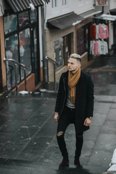 A vertical shot of a Caucasian fashionable sexy man with a brown scarf on the street background - 写真・画像