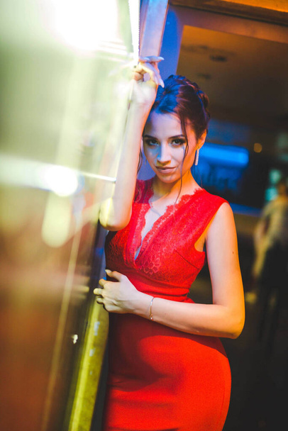An attractive young Caucasian female in a red dress posing while leaning on a wall in a restaurant - Foto, Imagem