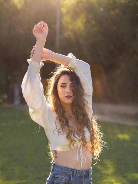 A young long-haired Spanish girl posing in the spring park with her arms up - Fotoğraf, Görsel