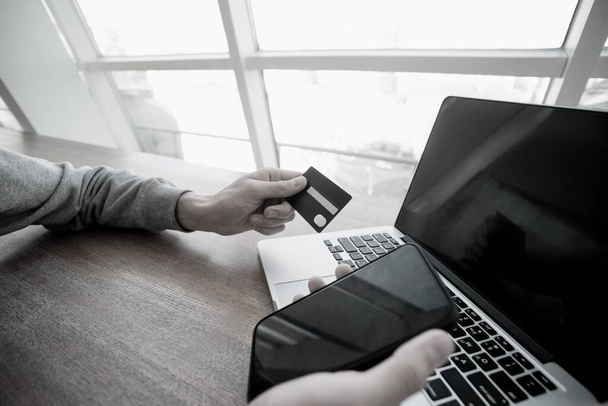 Male hands hold smartphone and credit card with laptop on background. Dont enter your credit card details on suspicious sites. Man using card to make an online purchase. Financial literacy concept - Photo, Image