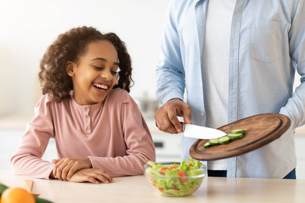 Cheerful afro father and daughter cooking salad together - Foto, Imagen