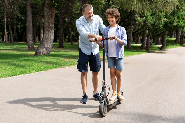 Boy learning to ride e-scooter with his adult dad - Foto, Imagem