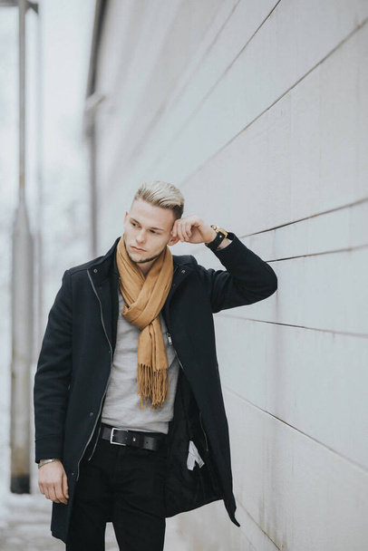 A vertical shot of a Caucasian fashionable sexy man with a brown scarf leaning on the wall - Фото, зображення
