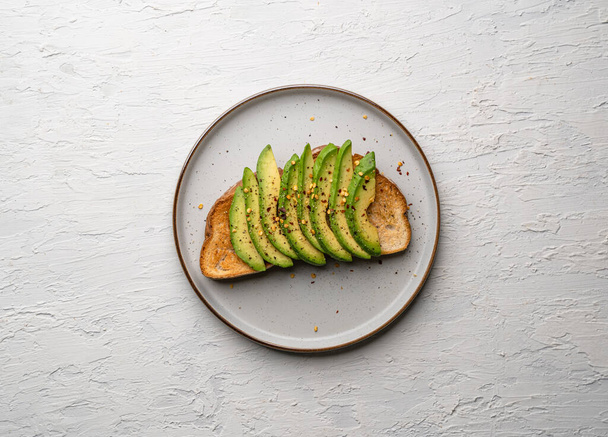 A top view of a delicious avocado toast on a white plate on a white surface - Photo, Image