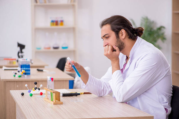 Young male chemist sitting at the desk in the classroom - Foto, Bild