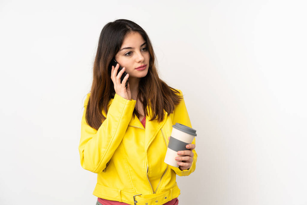 Jeune femme caucasienne isolée sur fond blanc tenant du café à emporter et un mobile - Photo, image