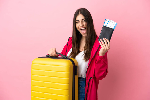 Giovane donna caucasica isolata su sfondo rosa in vacanza con valigia e passaporto - Foto, immagini
