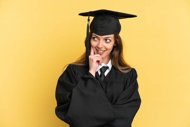 Young university graduate isolated on yellow background thinking an idea while looking up - Photo, Image