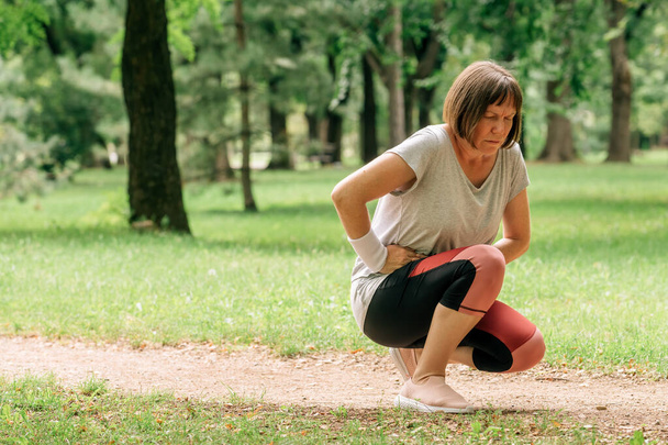 Female jogger with painful face grimace after feeling pain in lower abdomen during running in park - Φωτογραφία, εικόνα