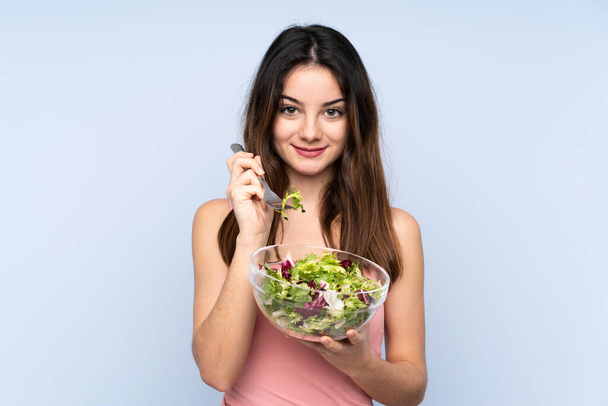 Young caucasian woman holding a salad isolated on blue background - Photo, Image