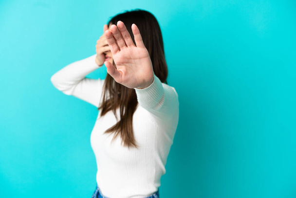 Young caucasian woman isolated on blue background making stop gesture and covering face - Fotoğraf, Görsel
