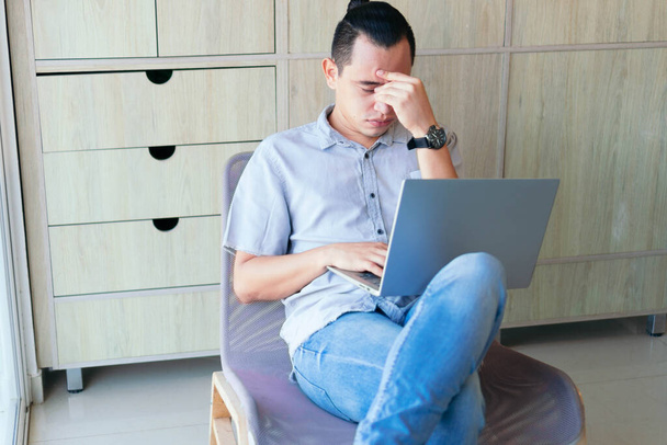 Een man die thuis werkt. Man gestrest tijdens het werken aan een laptop in zijn woonkamer. - Foto, afbeelding