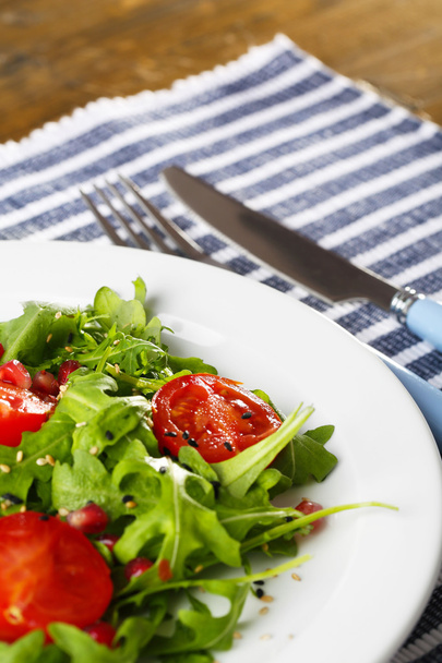 grüner Salat mit Rucola, Tomaten und Sesam auf Teller, auf Holzgrund - Foto, Bild