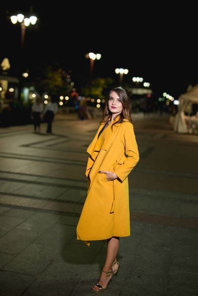 A vertical shot of a young blonde female model in a fashionable yellow coat - Foto, imagen