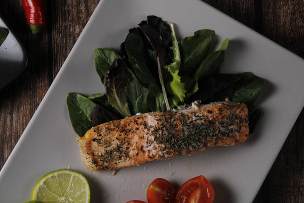 A plate of salmon fillet with spinach, lemon, and cherry tomatoes - 写真・画像
