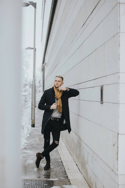A vertical shot of a Caucasian fashionable sexy man with a brown scarf leaning on the wall - Fotografie, Obrázek