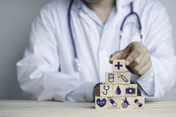 Lékařská ruka drží dřevěné stohování se zdravotnickými a nemocničními ikonami na stole, Zdravotní a pojišťovací koncepce. - Fotografie, Obrázek
