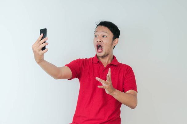 Wow face of Young Asian man shocked what he see in the smartphone on isolated grey background. - Фото, изображение