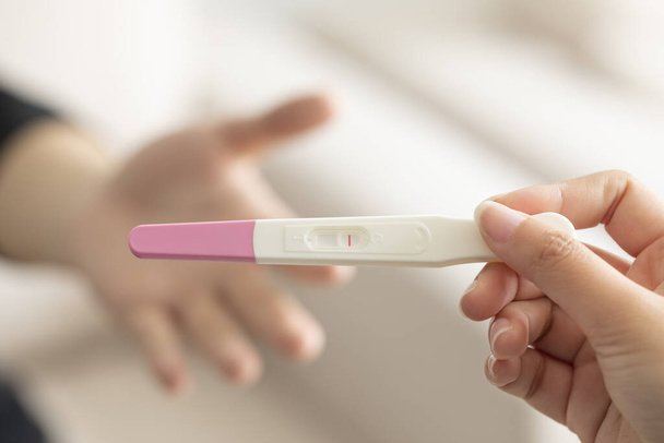 A closeup of a woman's hand holding up a pregnancy test kit with a negative result - Fotoğraf, Görsel