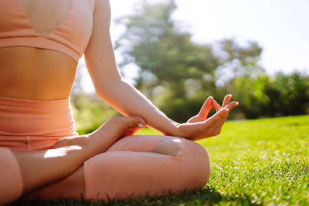 Parkta yoga yapan bir kadın. Yogacı kadın, doğada dinleniyor. Dişi lotus pozisyonunda oturuyor. Gün doğarken parkta meditasyon yapan kız. Sağlıklı yaşam tarzı. - Fotoğraf, Görsel