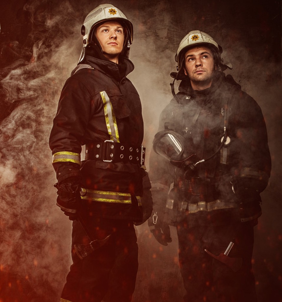 twee brandweerlieden met helm en bijl in een rook - Foto, afbeelding