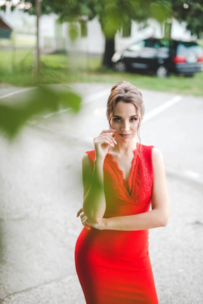 A sexy young Caucasian female in a red dress posing in a park - Foto, imagen