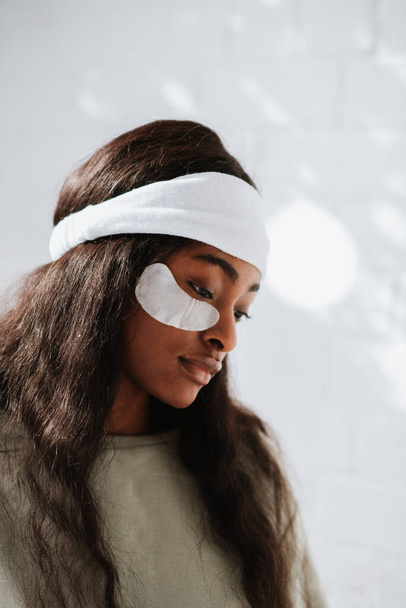 A side view of a young African female wearing a white headband with under-eye recovery patches at home - Fotó, kép