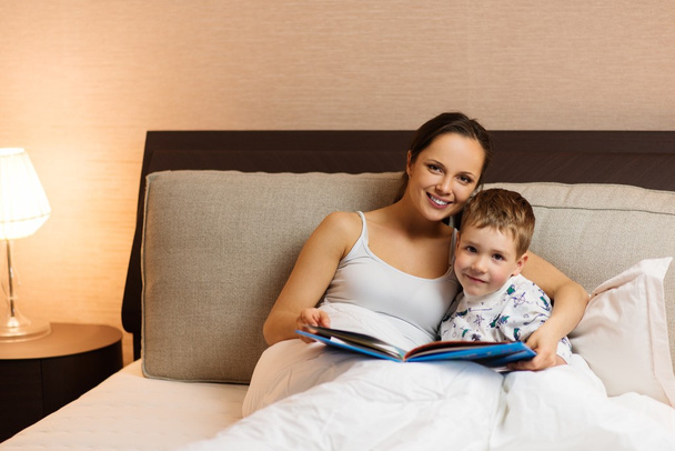 Молодая мать и ее сын читают книгу в постели
  - Фото, изображение