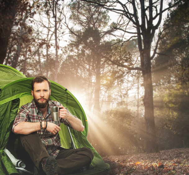 Красивый путешественник возле палатки с чашкой кофе в осеннем лесу
 - Фото, изображение